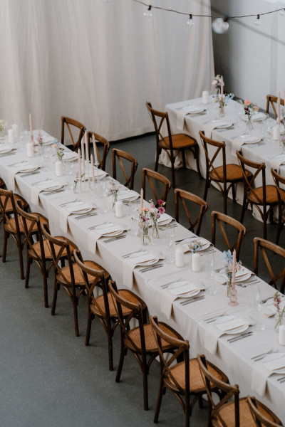 Lange gedeckte Tafeln in weiß für eine Hochzeit in einer minimalen Location