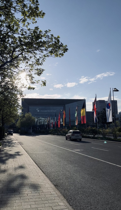 Blick auf ein Gebäude der Messe Frankfurt mit verschiedenen Flaggen entlag der Straße